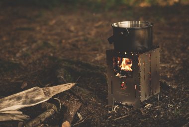 compact camping wood burning stove lit and with a pot on top