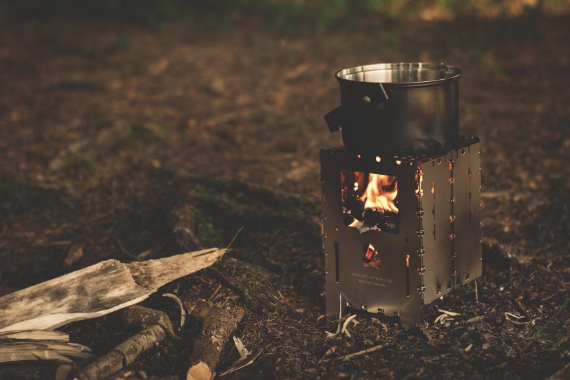 compact camping wood burning stove lit and with a pot on top