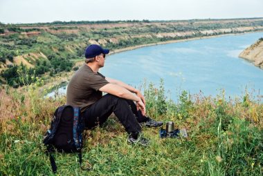 free solo camper, solo travel, wanderlust travel, summer vacations, eco tourism, outdoor backpacking. Male tourist with backpack sitting near camping stove with coffee. One man tourist hiker.