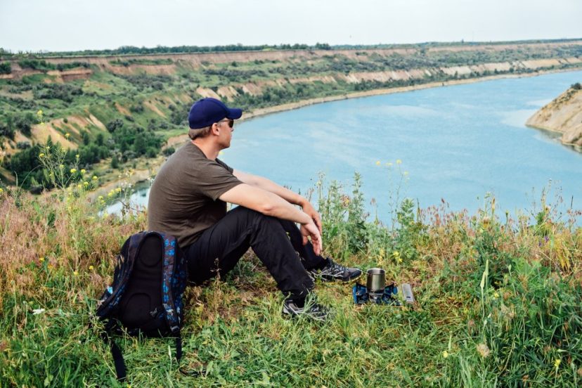 free solo camper, solo travel, wanderlust travel, summer vacations, eco tourism, outdoor backpacking. Male tourist with backpack sitting near camping stove with coffee. One man tourist hiker.