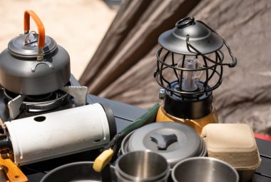 Essential Accessories for a Pop Up Camper. Cooking gear for a tranquil beach campsite, kettle, pot, pan, gas stove, flashlight, and camera set on a table by the tent. Cooking gear for a tranquil beach campsite, kettle, pot, pan, gas stove, flashlight, and camera set on a table by the tent.