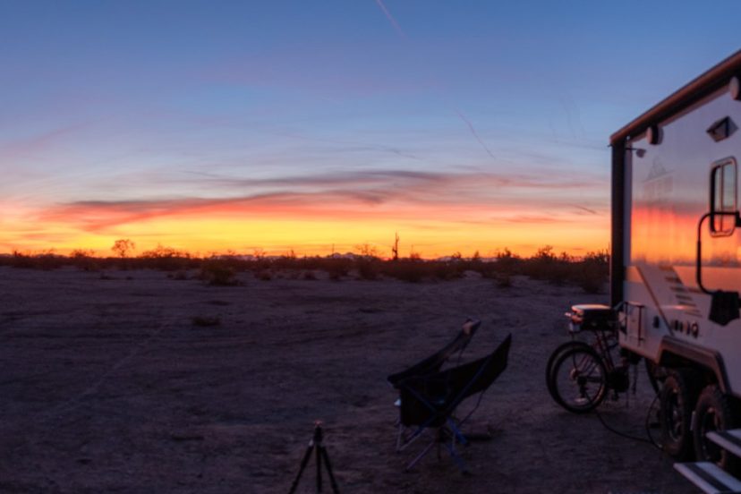 A blue truck is parked alongside a Wolf Pup Camper in an idyllic rural setting surrounded by lush greenery