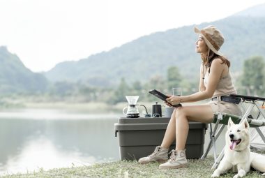 Young woman camping alone out doors with her dog, using digital tablet.