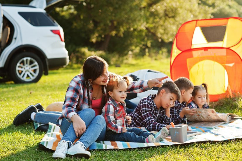 Mother with four kids outdoor in picnic blanket against their american suv.