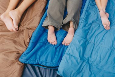 Three people, an adult and two boys lying on sleeping bags, knees down, bare feet.