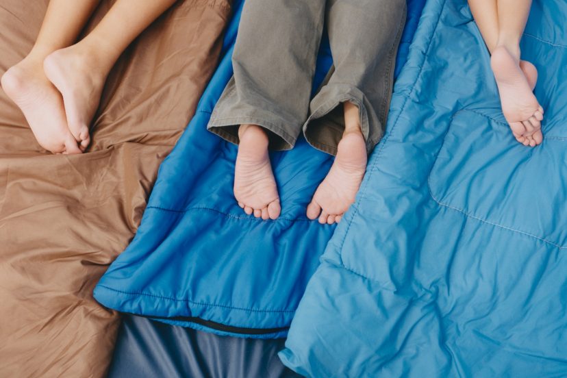 Three people, an adult and two boys lying on sleeping bags, knees down, bare feet.