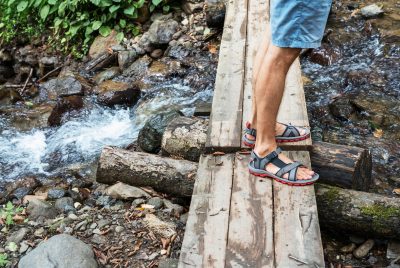 men's feet in sandals on a wooden bridge across a mountain river